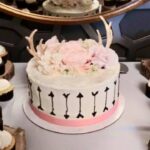 A cake with arrows and cupcakes on a table.