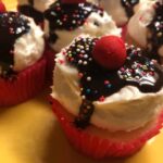 Cupcakes topped with chocolate icing and sprinkles on a yellow plate.