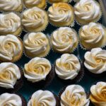 A box of cupcakes with white frosting and gold sprinkles.