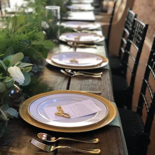 A long table set with gold plates and greenery.